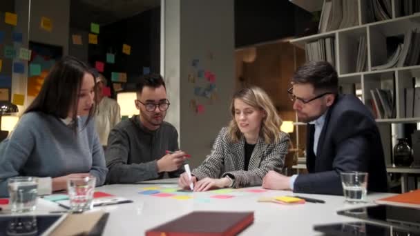 Tvůrčí týmoví designéři pracují na novém projektu, sdílení nápadů, psaní informací o barevných samolepkách. Skleněná kancelářská zeď s jasnými poznámkami je na pozadí. — Stock video
