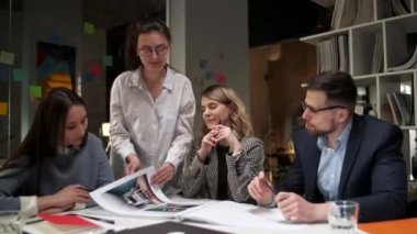 Yaratıcı tasarımcılardan oluşan bir ekip proje dergisine bakıyor, onlar hakkında konuşuyor, masada birlikte oturuyorlar. Modern Gayri Resmi Ofis. Dostane Çalışma Ortamı