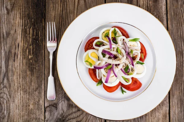 Салат с кальмарами, яйцом и помидорами на белой тарелке на фоне — стоковое фото