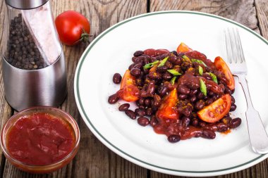 Kuru fasulye, domates, ketçap, soğan ve baharat beyaz plat üzerinde