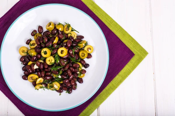 Салат с красной фасолью и зелеными оливками в миске на белых досках — стоковое фото