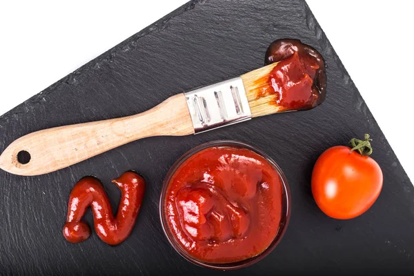 Bol avec ketchup, tomates et brosse sur fond de pierre noire — Photo