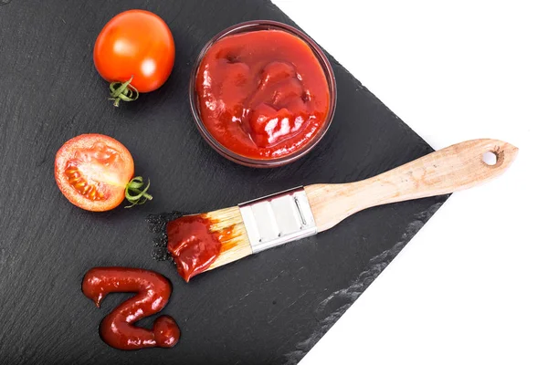 Bol avec ketchup, tomates et brosse sur fond de pierre noire — Photo