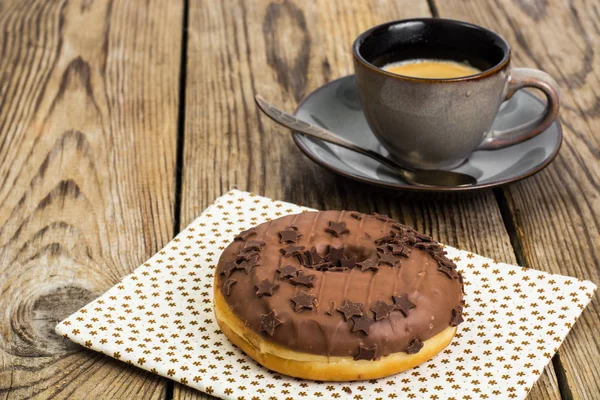 Een donut in chocolade glazuur op houten achtergrond — Stockfoto