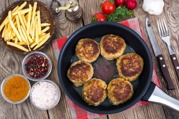 Картошка фри на деревянной тарелке и котлеты с жареным мясом на сковородке — стоковое фото