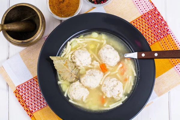 Soup with noodles and meatballs in ablack plate — Stock Photo, Image