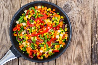 Ahşap masa üzerinde tavada karışık sebze pişmiş
