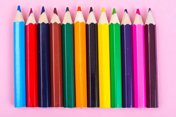 Разноцветные карандаши на фоне розовой бумаги — стоковое фото