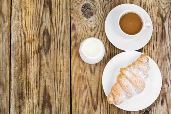 El desayuno. Croissant fresco y taza de café con leche sobre madera — Foto de Stock