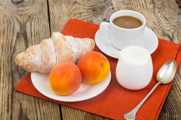 El desayuno. Croissant fresco y taza de café con leche sobre madera — Foto de Stock