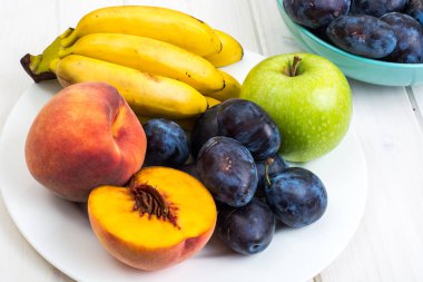 Çeşitli olgun taze Erik, muz, şeftali ve beyaz masada elma