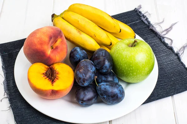 Çeşitli olgun taze Erik, muz, şeftali ve beyaz masada elma