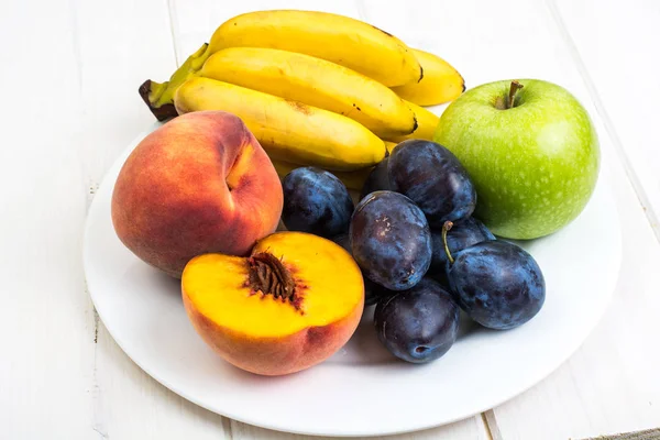Çeşitli olgun taze Erik, muz, şeftali ve beyaz masada elma