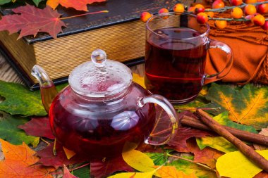 Aromatik kırmızı çay, kitap, ahşap masa üzerinde renkli sonbahar yaprakları