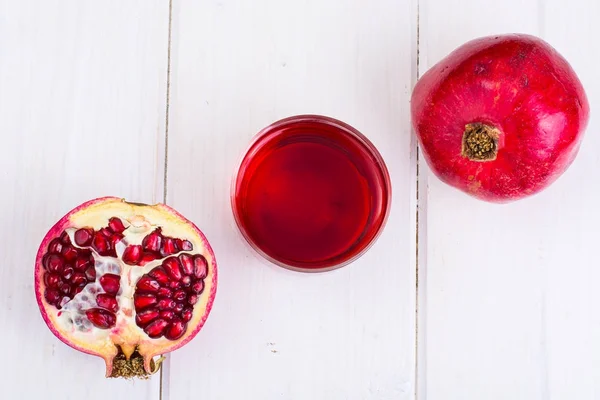 Pomegranate and juice in glass on white wooden background — Stock Photo, Image