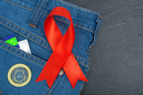 Red ribbon and condom on blue jeans background. Concept of awareness and protection against AIDS, HIV. 1 December