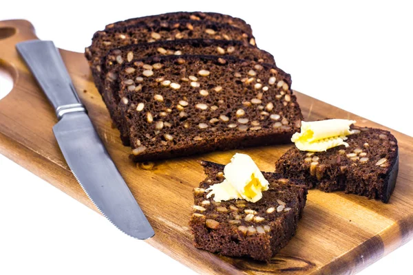 Pão de centeio com grãos e manteiga em tábua de cozinha de madeira — Fotografia de Stock