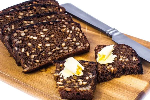 Pão de centeio com grãos e manteiga em tábua de cozinha de madeira — Fotografia de Stock