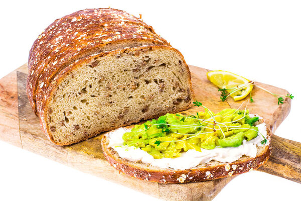 Slice of whole wheat bread with avocado and goat cheese on wooden board. Studio Photo