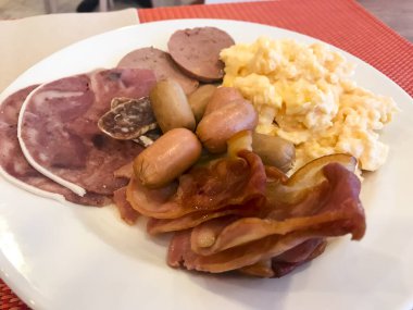 Tabakları kahvaltı masasına koyun. Çırpılmış yumurta, omlet, börek, kruvasan, şampiyon, kıtır pastırma, sosis. Üst görünüm 