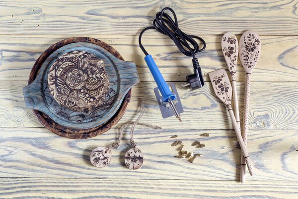 A set of tools for burning wood with nozzles and examples of wooden objects with drawings on a wooden table close-up