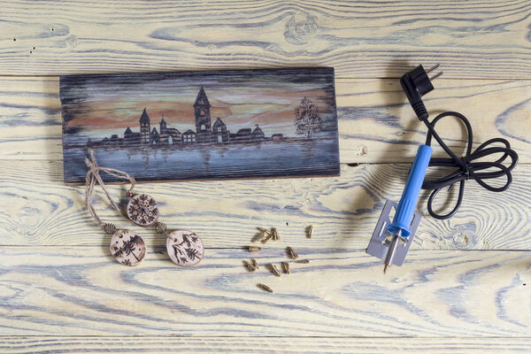 A set of tools for burning wood with nozzles and examples of wooden objects with drawings on a wooden table close-up