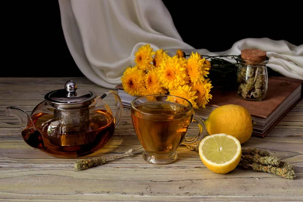 Useful herbal tea with a plant (Sideritis scardica) or Greek mountain tea with lemon in a cup and yellow chrysanthemums on a wooden table  close-up