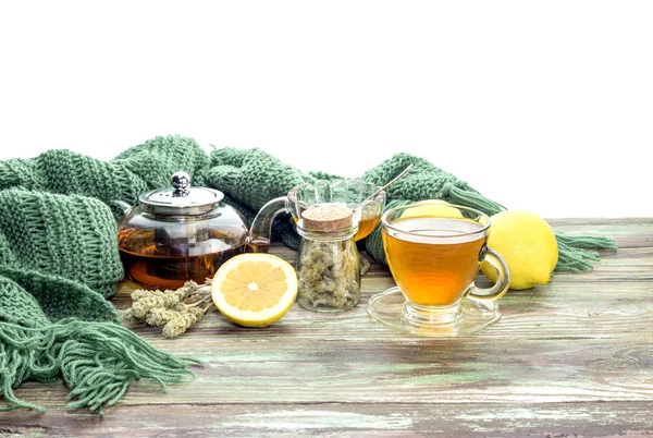Useful herbal tea with a plant (Sideritis scardica) or Greek mountain tea with lemon in a cup and yellow chrysanthemums on a wooden table close-up