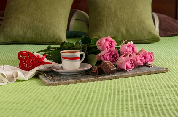 A tray with a cup of coffee, sweets and a bouquet of pink roses lie on the bed to the day Valentine\'s Day