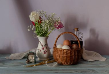 Paskalya natürmort. Yumurta bir hasır sepet, Lale buketi, ahşap masa yakın çekim simgesi ve kilise mum.
