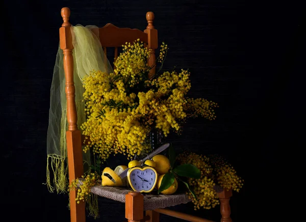 仍然生活与新鲜的树枝含羞草 柠檬和黄色的时钟在一个木椅关闭 — 图库照片