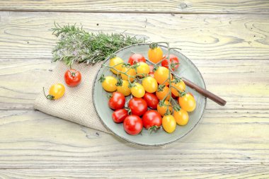 Bir tabak, dal biberiye ve ahşap arka plan yakın çekim üzerinde bir bıçak sarı ve kırmızı kiraz domates