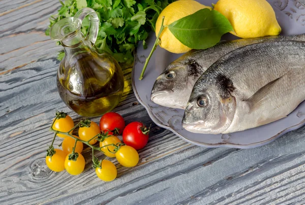 Healthy eating. Fish sea breams(Sparus aurata) on a plate, lemons and cherry tomatoes on a wooden table close-up.