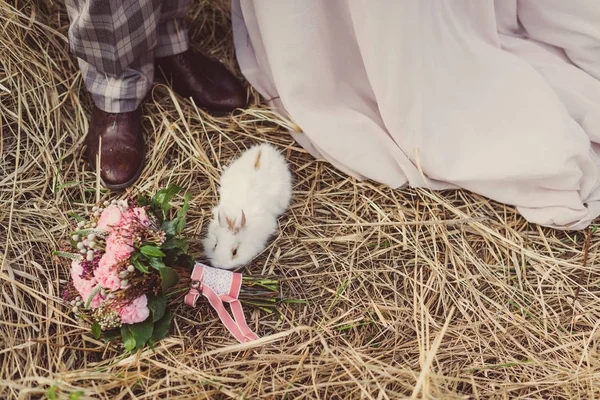 Білий кролик біля букета і ніг молодої пари . — стокове фото