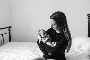Genç bir anne yeni doğmuş bir bebeği kollarında tutuyor ve ona bakarken gülümsüyor. Kollarında anne ve bebeğin siyah-beyaz fotoğrafı..