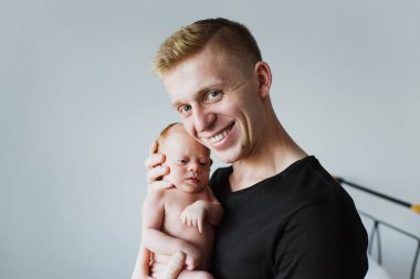 Genç baba yeni doğmuş bir bebeği kollarında tutuyor ve kameraya bakıyor. Genç baba yeni doğmuş bir çocuğu kollarına alıp gülümsüyor..