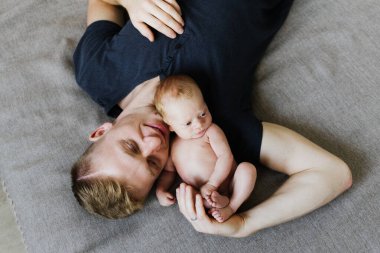 Genç baba yeni doğmuş bir bebeği yatakta kucaklıyor. Genç baba yeni doğan oğluna sarılıyor..