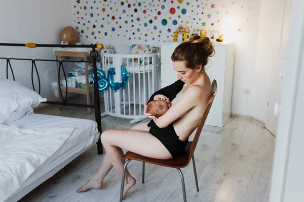 一位年轻漂亮的母亲坐在儿童房的椅子上给新生儿喂奶 — 图库照片