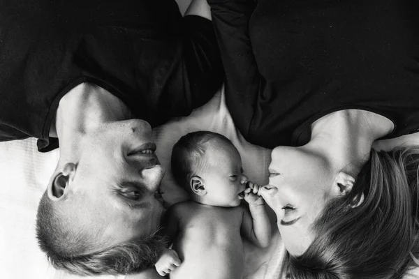年轻父母抱着新生儿躺在床上的黑白照片 — 图库照片