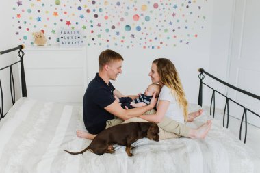 Bebeği ve köpeği olan genç bir aile yatakta oturuyor ve sarılıyorlar, gülüyorlar..