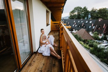 Çarşaflı genç bir adam ve kadın ellerinde şampanya bardaklarıyla balkonda oturuyorlar..