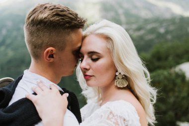 Boho tarzı elbiseler içindeki güzel gelin, dağlarda şapka ve damat sarılıyor..