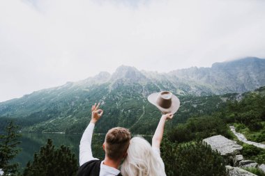 Boho tarzı bir elbise içinde güzel bir gelin, şapka ve damat sarıl ve dağlarda ellerini göster..