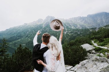 Boho tarzı bir elbise içinde güzel bir gelin, şapka ve damat sarıl ve dağlarda ellerini göster..