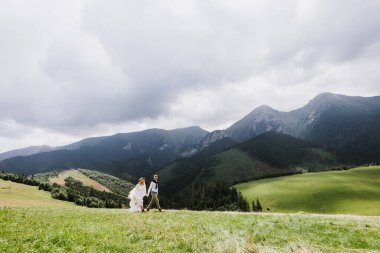 Boho tarzı elbise, şapka ve damat giymiş güzel gelin dağlarda koşup gülüyor..