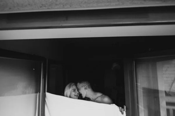シーツで閉じながら若い男と女が笑っている そうだ 家の窓の近くのシーツに身を包んだ男と女の白黒写真 — ストック写真