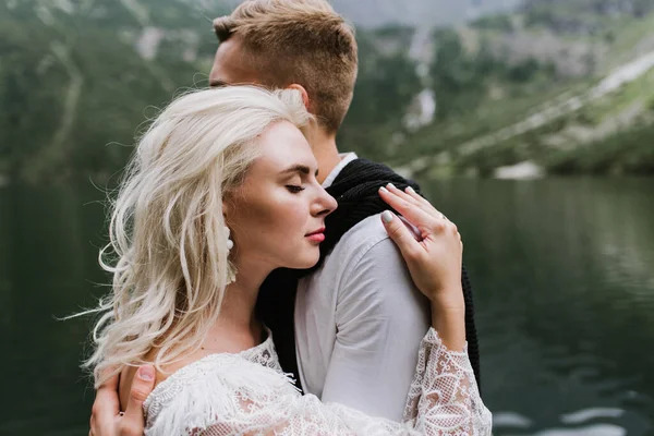 美丽的新娘穿着紧身衣和新郎 在山中的一个湖边笑着 新娘和新郎在山里拥抱 — 图库照片