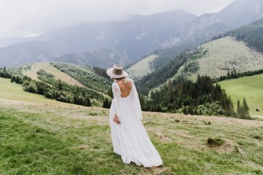 Şapkalı ve boho elbiseli güzel bir kadın dağlarda yürüyor. Güzel gelin dağlarda yürüyor.