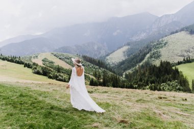 Şapkalı ve boho elbiseli güzel bir kadın dağlarda yürüyor. Güzel gelin dağlarda yürüyor.