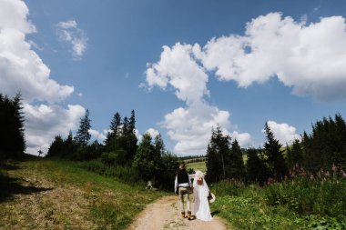 Boho tarzı bir elbise içindeki güzel gelin ve damat ormanda yolda yürüyor..